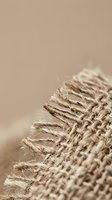 Natural jute burlap fabric texture with frayed edges and woven fibers in neutral beige tones for rustic crafting and eco-friendly design projects.