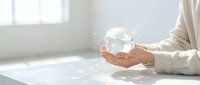 Hands holding transparent crystal sphere on white surface with natural light from window, symbolizing future vision and business strategy.