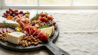 Gourmet charcuterie board with assorted meats, cheeses, nuts, grapes and crackers arranged on wooden serving platter for entertaining and appetizers.