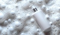 White cosmetic bottle with pump dispenser floating in luxurious foam bubbles on light background, mockup for skincare and beauty products presentation.