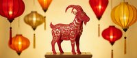 Red paper cut goat silhouette with traditional ornamental patterns on wooden stand surrounded by colorful hanging lanterns for Chinese New Year celebration.