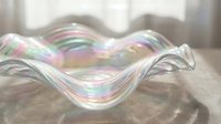 Iridescent glass bowl with wavy edges displaying rainbow reflections on wooden surface in soft natural light for home decor and tableware design.