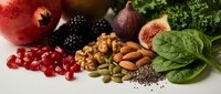 Antioxidant-rich superfoods including pomegranate, berries, nuts, seeds and leafy greens arranged on white background for healthy nutrition concepts.