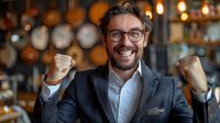 Successful businessman celebrating victory with raised fists in modern restaurant. Professional portrait of young male entrepreneur showing excitement and achievement in corporate setting.