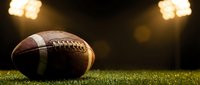 American football on green grass field under bright stadium lights creating dramatic sports atmosphere for game day excitement and competition.