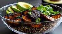 Grilled teriyaki glazed sweet potato slices on quinoa base with fresh avocado and green onions in glass bowl, close up view of healthy plant based meal.