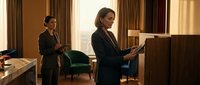 Two professional businesswomen in dark suits working in elegant hotel room or executive office space reviewing documents and using mobile technology.