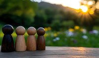 Wooden pawn figures standing together on rustic surface against blurred nature background with sunset rays, symbolizing unity, diversity and teamwork.