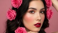 Young woman with dark hair and red lipstick surrounded by pink roses on pink background. Beauty portrait with floral elements for cosmetics and fashion.