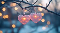 Glowing pink heart ornaments hanging on winter tree branch with soft bokeh lights in background, creating romantic Valentine's Day atmosphere.