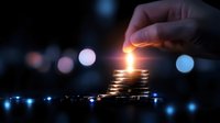 Stack of golden coins with glowing candle on top in dark setting with bokeh lights background, symbolizing financial growth and investment success.