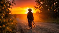 Silhouetted figure in hat walking on rural dirt road at golden sunset with glowing sky and blurred foliage framing scene, conveying solitude and journey themes for travel and lifestyle content.