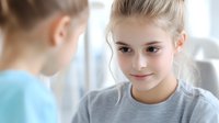 Young caucasian girl with blonde hair in gray t-shirt smiling warmly during conversation. Soft natural lighting creates gentle atmosphere for lifestyle and education concepts.