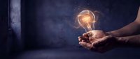 Hands holding glowing lightbulb with sparkling energy against dark background, representing innovation, creativity, ideas, and business solutions.