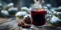 Steaming mulled wine in glass mug with spices on rustic wooden table surrounded by snowy pine branches and cones, creating cozy winter atmosphere.