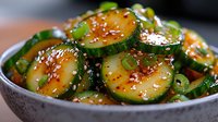 Fresh cucumber salad with sesame seeds and green onions in spicy Asian dressing, served in ceramic bowl. Close up view of marinated vegetable appetizer.