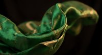 Luxurious emerald green silk fabric flowing gracefully with golden highlights against dark background for fashion and textile design projects.