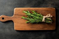 Fresh rosemary sprigs tied with twine on rustic wooden cutting board against dark background, overhead view for food and cooking blogs.