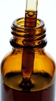 Amber glass dropper bottle filled with golden liquid, pipette dispensing essential oil or serum for skincare, cosmetics, and wellness product packaging.