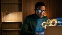African American male engineer working late at computer with holographic gears display in modern office environment for technology innovation projects.