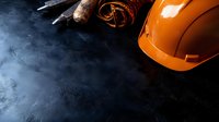 Orange protective hardhat and rusty metal tools on dark concrete background with copy space, construction industry concept for safety workplace.