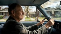 Senior Caucasian man driving car through residential neighborhood, elderly driver behind steering wheel enjoying peaceful ride on suburban street.
