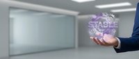 Professional businessman in dark suit holding glowing purple holographic stable text sphere in modern minimalist office interior with glass walls.