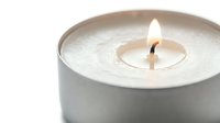 Lit white candle in a minimalist metal tin with a glowing flame, soft light, and clean aesthetic for wellness and home decor.