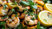 Grilled jumbo shrimp garnished with fresh herbs, basil leaves and lemon slices on dark background. Close up view of succulent seafood with charred marks.
