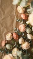 Easter arrangement with pastel painted eggs and delicate ranunculus flowers on kraft paper background for spring holiday decorating and seasonal crafts.