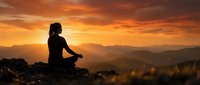 Woman silhouette meditating in lotus pose on mountain peak during golden sunset with dramatic orange sky and layered mountain ranges in background.