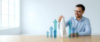 Professional businessman in glasses analyzing growth chart with upward trending arrows on wooden desk in modern office environment for business success presentations.