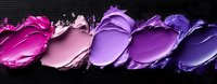 Crushed makeup eyeshadow or lipstick samples in gradient shades from bright pink to deep purple arranged in artistic smears on dark background.