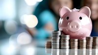 Pink ceramic piggy bank with stacks of silver coins showing increasing financial growth trend against blurred background with bokeh lights.