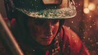 Dramatic portrait of young Caucasian male firefighter in protective helmet with water drops and sparks in dark atmospheric lighting during rescue operation.