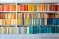 Colorful books arranged by spectrum on white bookshelf, creating rainbow gradient from red to blue, organized by color for aesthetic display.