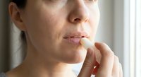 Woman applying lip balm for dry chapped lips skincare routine natural light close-up beauty treatment moisturizing cosmetics self-care wellness.