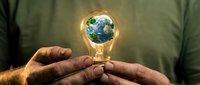 Hands of a man holding a glowing light bulb with Earth and green trees inside, symbolizing eco innovation and sustainable energy concept.