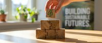 Hand placing wooden block with tree symbol on stacked cubes representing sustainable development and environmental responsibility in bright office.