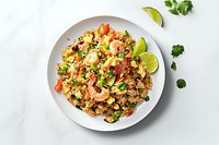 Asian shrimp fried rice with vegetables, eggs and lime garnish served on white plate against marble background. Fresh herbs add vibrant color.