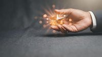 Businessman hand holding glowing lightbulb with sparkling particles representing innovation, creativity and bright ideas for business solutions.