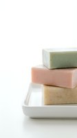 Stack of three handmade soaps in green, pink, and natural tones on white ceramic tray. Isolated on white background, ready for spa, wellness, and beauty product design use.