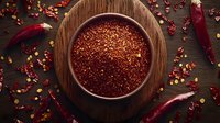 Ground red chili pepper flakes in wooden bowl on dark rustic table with scattered dried peppers, top view composition for cooking and seasoning.