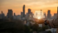Hand holding glowing light bulb against blurred city skyline at sunset. Innovation and creative thinking concept for business solutions and bright ideas.