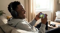 Young African American man enjoying mobile gaming with headphones on comfortable sofa in bright modern living room for entertainment and leisure activities.
