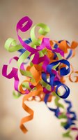 Colorful curly ribbon streamers in pink green orange and blue creating festive party decoration against neutral background for celebrations and events.