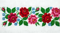 Cross stitch embroidery border with red and pink roses, green leaves and blue flowers on white fabric. Traditional needlework pattern for crafts and decoration.