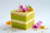 Green tea matcha layered cake square slice with white cream frosting decorated with edible flowers on white background for bakery menu design.