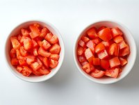 Fresh diced red tomatoes in two white ceramic bowls on light background, top view. Raw vegetable preparation for cooking and salads.