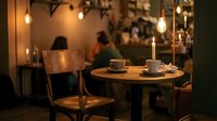 Cozy cafe interior with warm lighting, wooden table and chairs, coffee cups and candle creating intimate dining atmosphere for restaurants and hospitality.